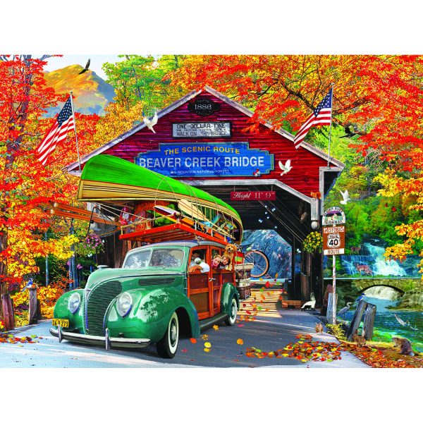 A green vintage car carrying a canoe drives through a red covered bridge with a sign reading "Beaver Creek Bridge" amid vibrant autumn foliage. American flags and birds are also visible in the RoseArt - Kodak Cork - Covered Bridge - 1000 Piece Jigsaw Puzzle.